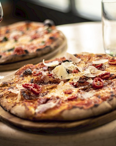 Two pizzas on wooden platters, garnished with cheese and tomatoes, accompanied by a glass of red wine and a green bottle on a table.