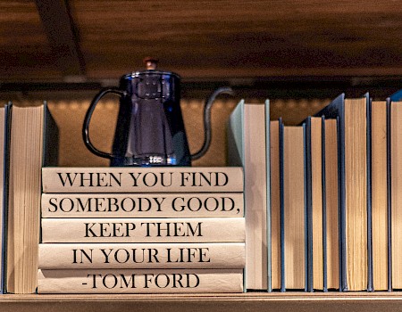 A shelf with books and a teapot on top. Books stacked in the center display the quote: 