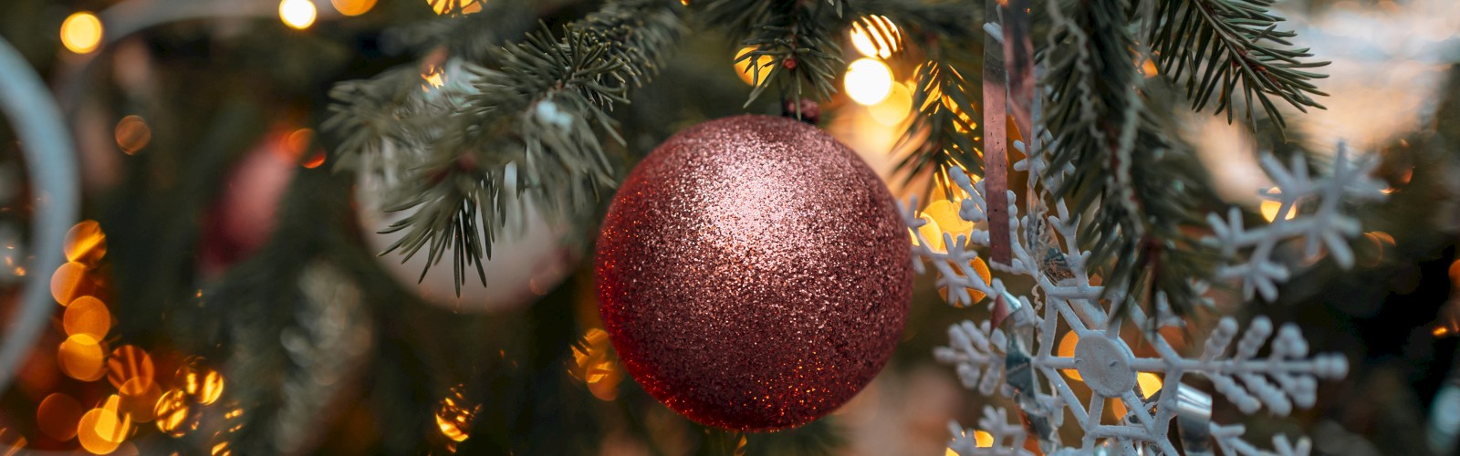 A Christmas tree decorated with a red ornament, snowflake decoration, and glowing lights in the background, creating a festive atmosphere.