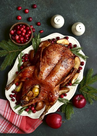 A roasted turkey garnished with cranberries and herbs, surrounded by apples and candles, on a festive table setting.