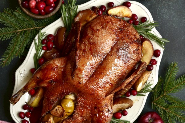 A roasted turkey garnished with cranberries and herbs, surrounded by apples and candles, on a festive table setting.
