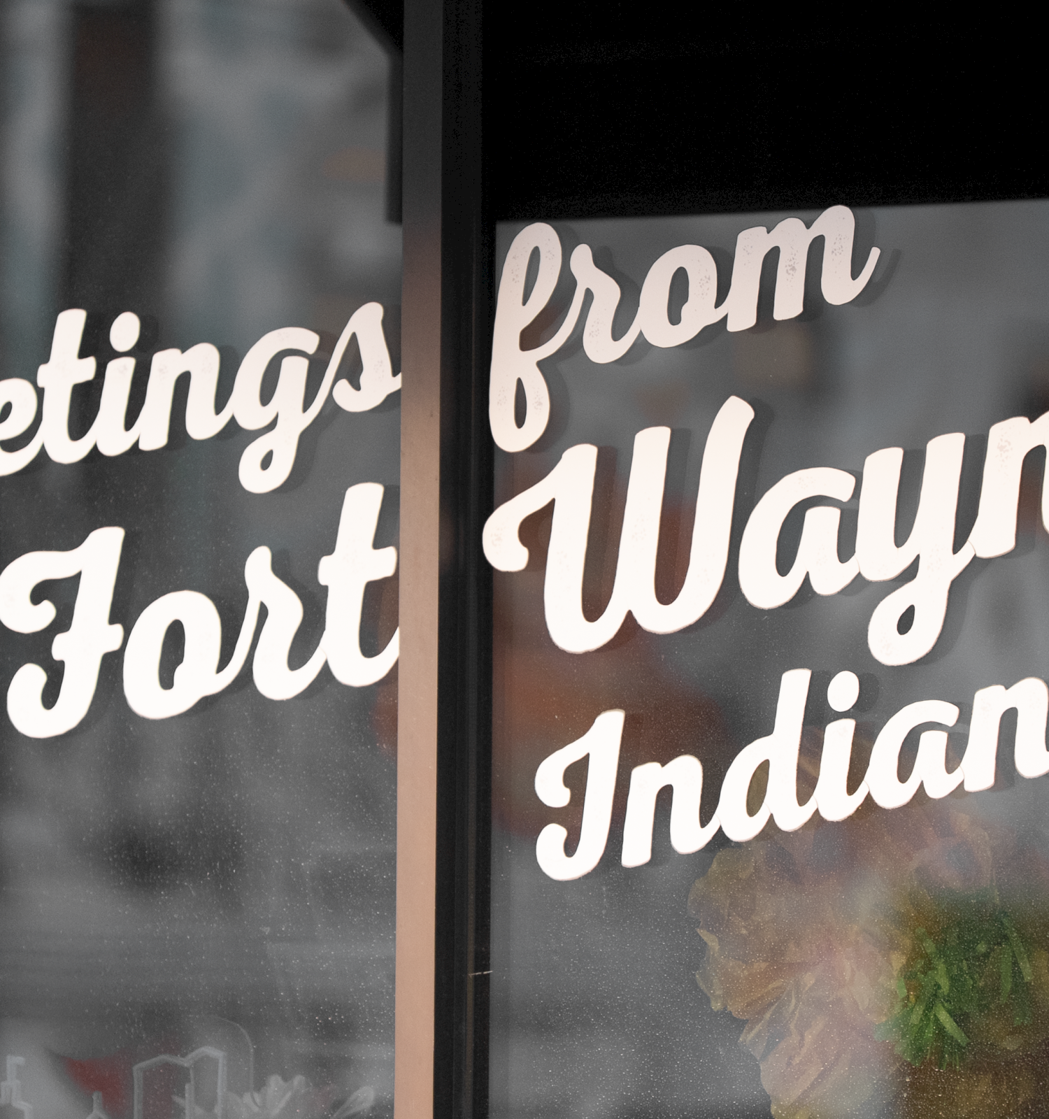 Greetings from Wayne, Indiana—faded window signage with retro cursive text on glass, saying “Greetings from Wayne Indiana.”