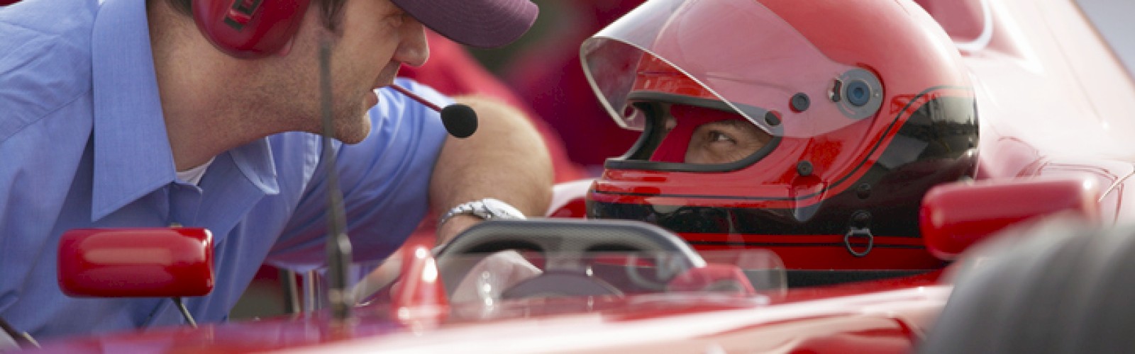 A race car driver in a helmet listens to a team member with a headset before a race.