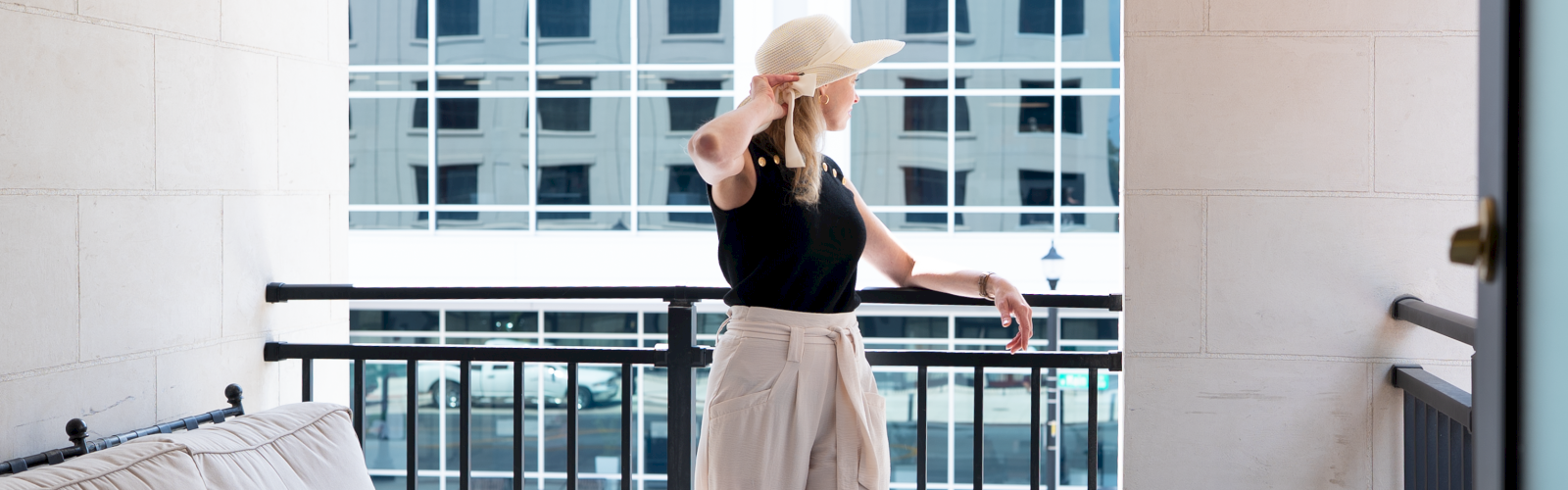 A woman wearing a hat looks out over a balcony in a modern urban setting.